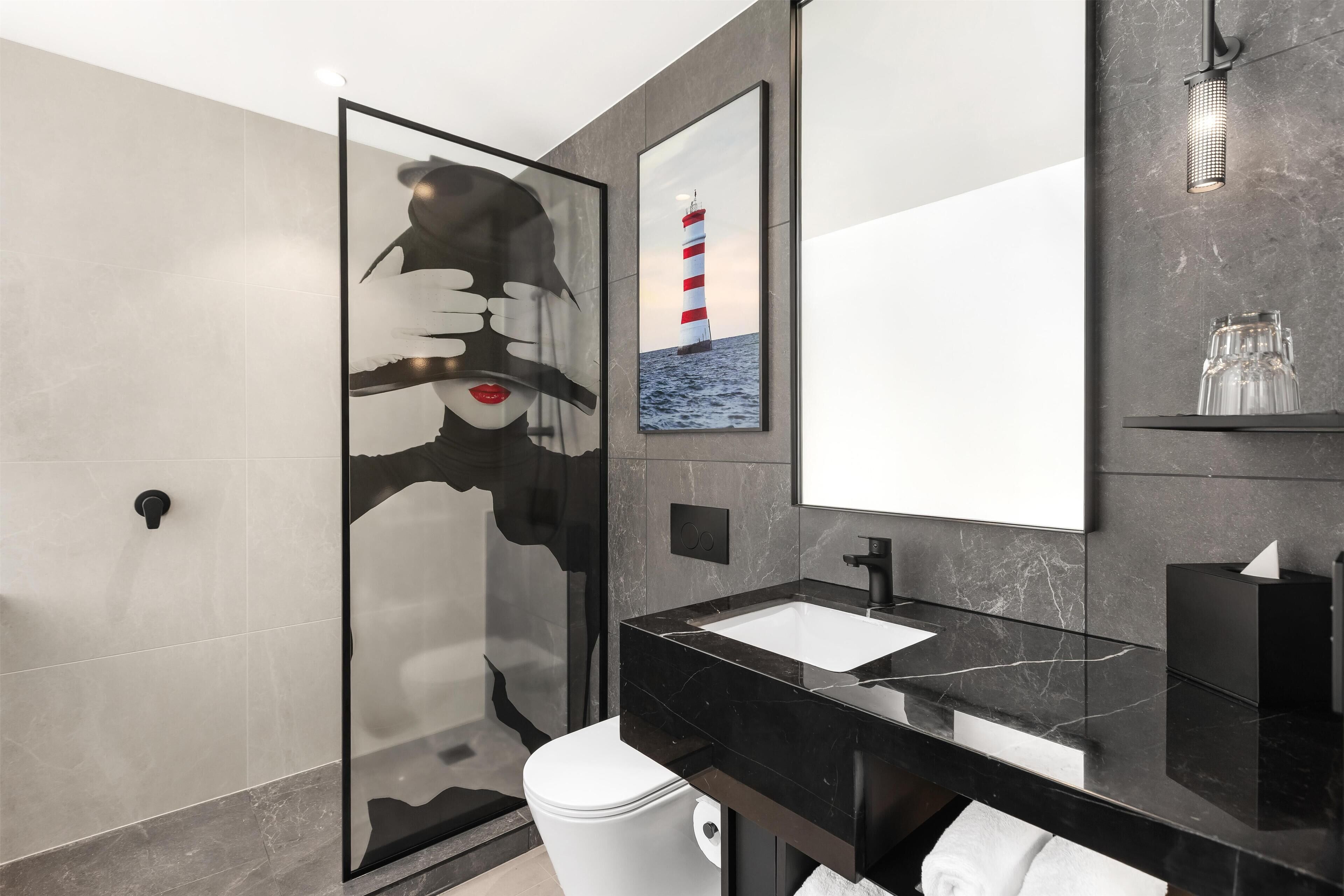 A modern bathroom with a glass shower enclosure, a black marble sink, and a large mirror.