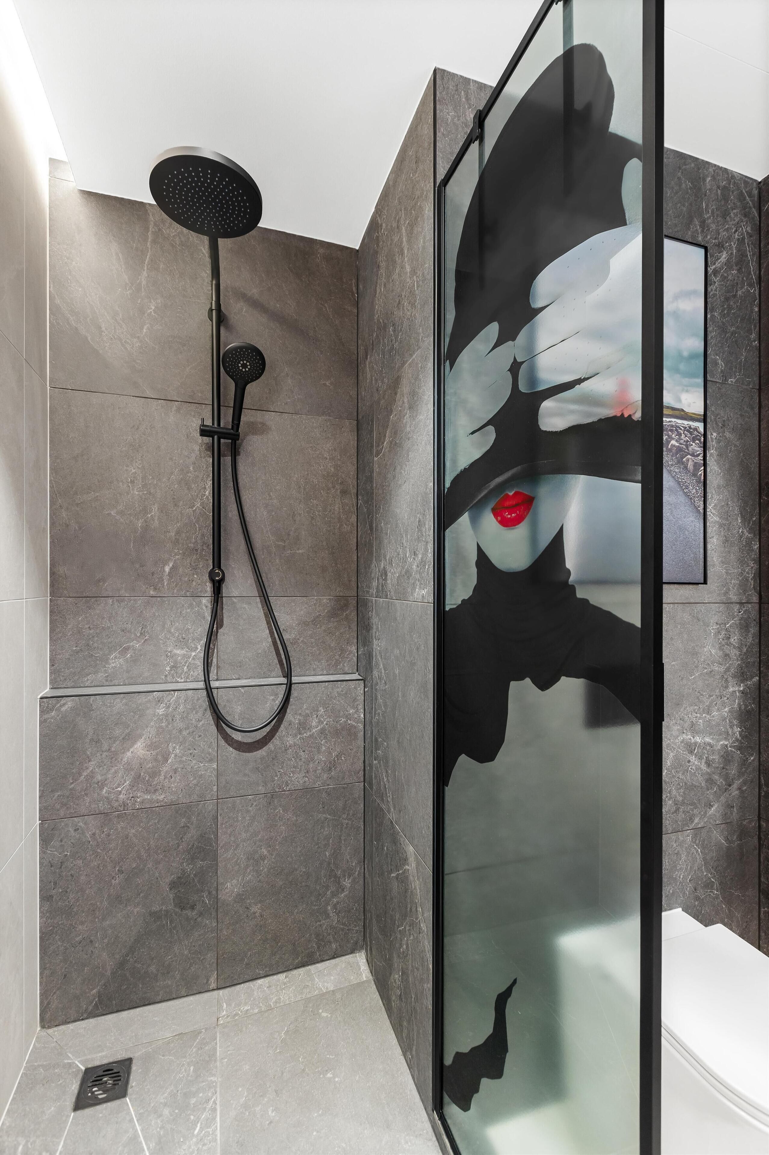 A modern bathroom with a glass shower enclosure, a handheld showerhead, and a wall-mounted control.