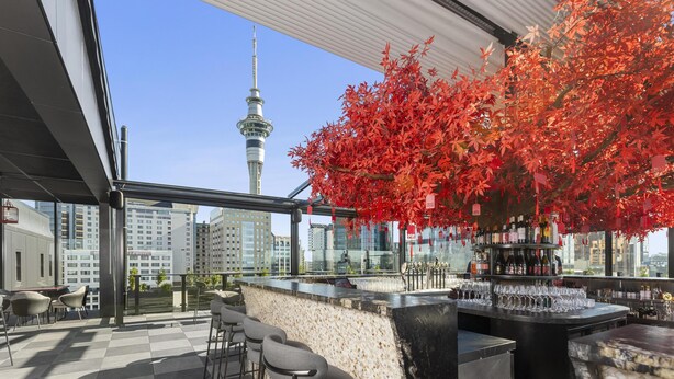 Un bar situé sur un toit, offrant une vue sur la ville, une haute tour et un arbre aux feuilles rouges.
