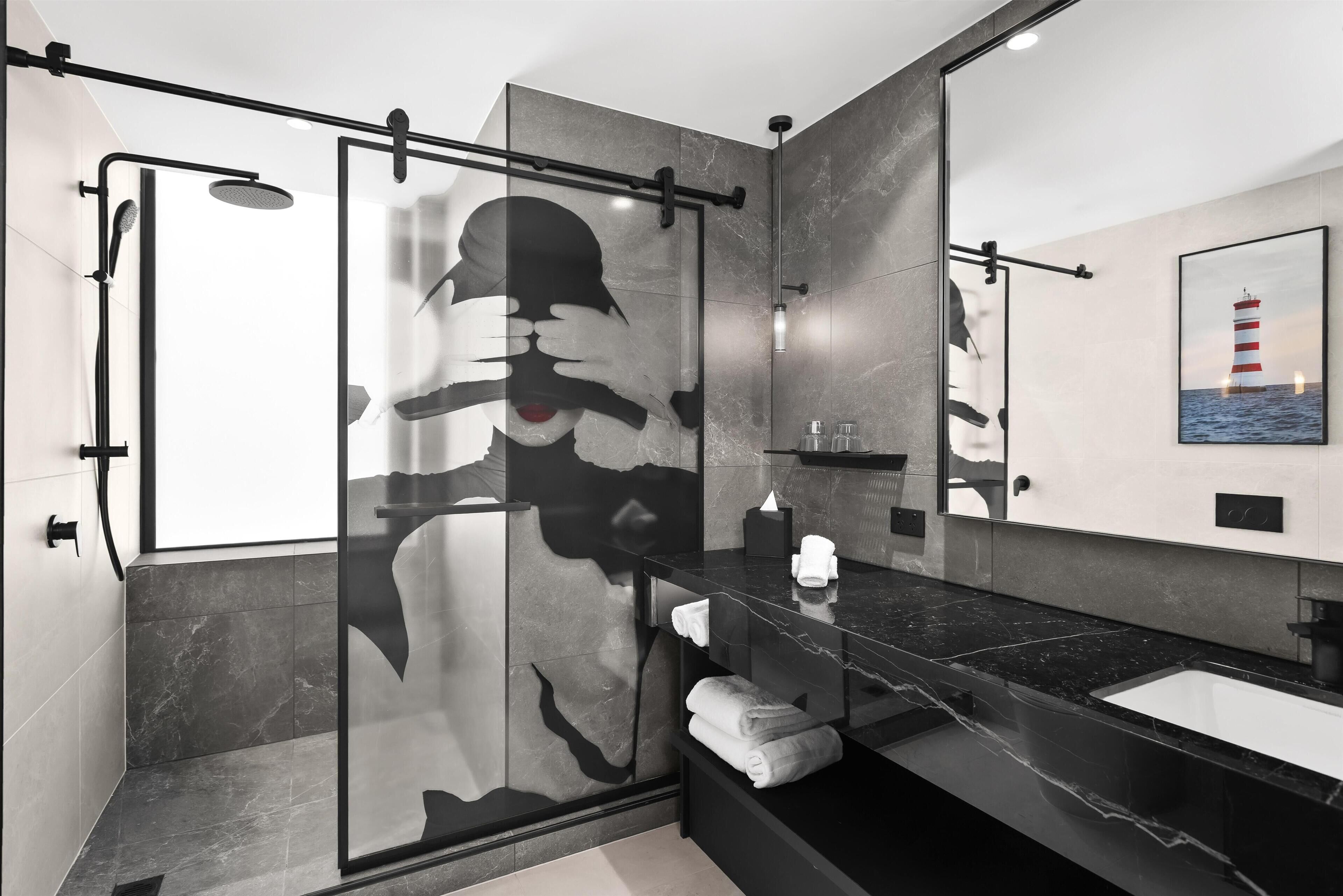 Une salle de bain moderne avec une douche à parois de verre, un comptoir en marbre noir et un grand miroir.