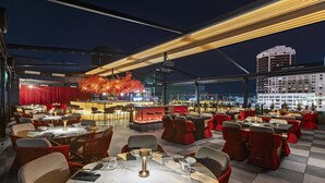 Un espace extérieur aménagé pour les repas, avec des tables et des chaises, un foyer et une vue sur le paysage urbain illuminé la nuit.