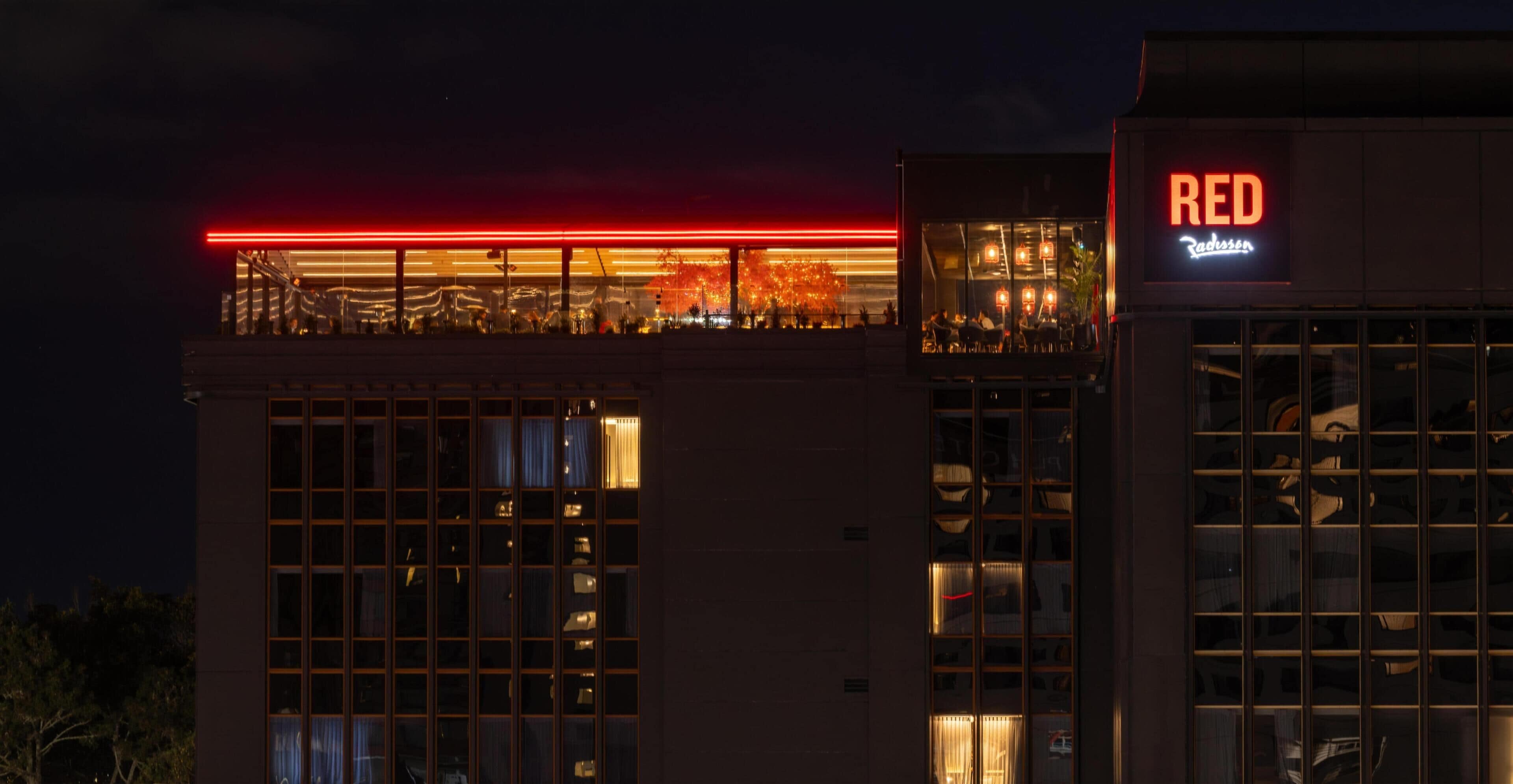 A building with a red neon sign, large windows, and a balcony with railings.