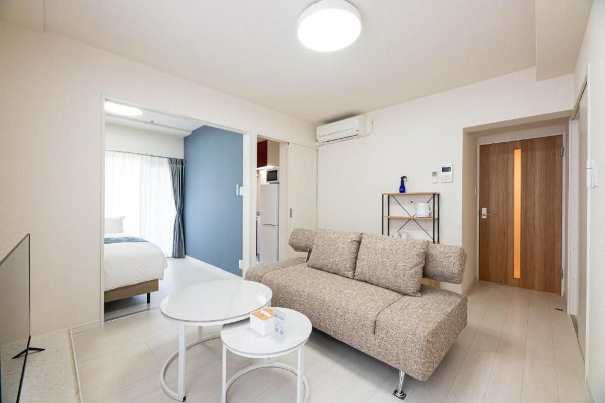 A hotel room with a bed, a sofa, a small table, a TV, and a door leading to another room.