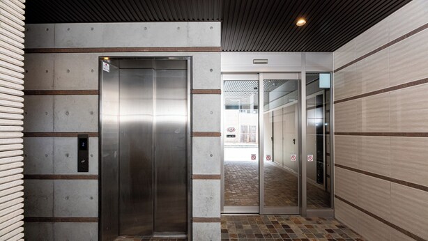 An elevator with a metallic finish, a tiled floor, and a wall with a grid pattern. - SPAZIO 6 Hakata Station (Fukuoka)