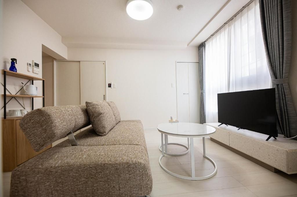 Un salon moderne avec un canapé, une table ronde, un téléviseur à écran plat et une fenêtre avec des rideaux.