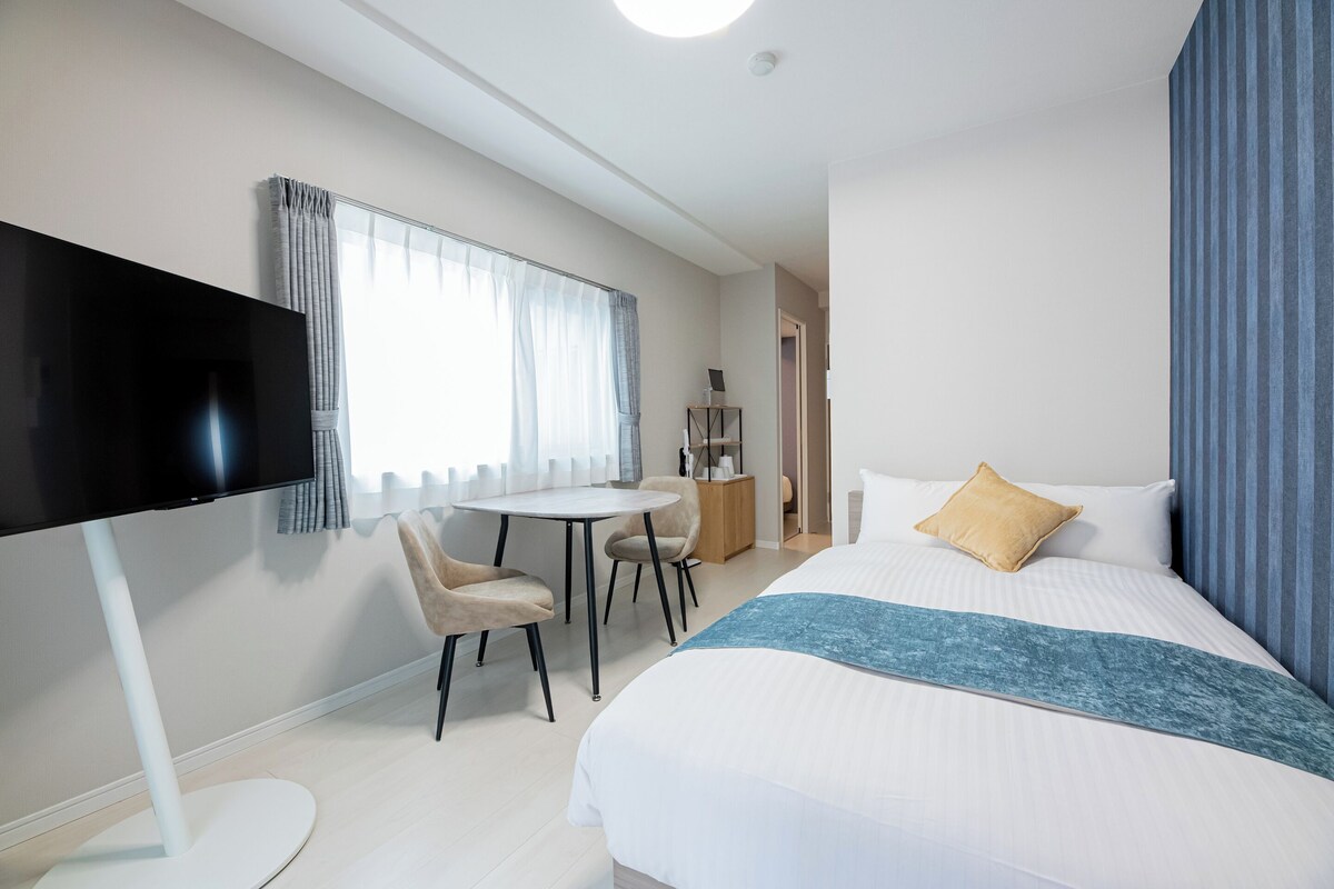 A modern hotel room with a bed, a TV, a desk, and a chair.