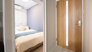 A bedroom with a bed, a wooden door, and a ceiling light. - SPAZIO 6 Hakata Station (Fukuoka)