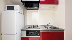 A compact kitchen with a white refrigerator, a microwave, a gas stove, and a built-in oven. - SPAZIO 6 Hakata Station (Fukuoka)