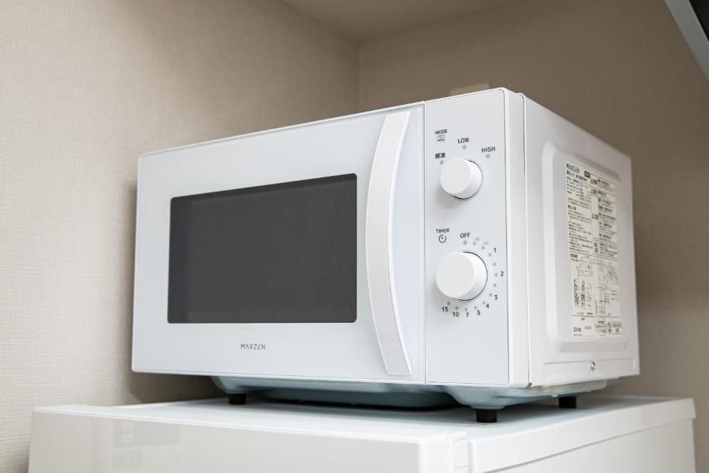 En hvid mikrobølgeovn med digitalt display og knapper, stående på en hvid overflade.