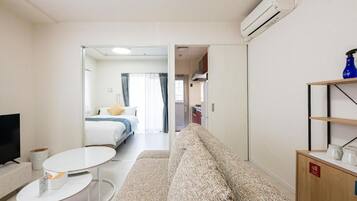 A hotel room with a sofa, a small table, a TV, and a bed with a window.