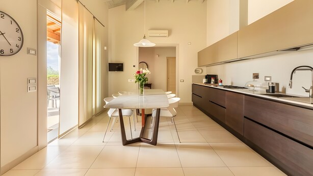 A modern kitchen with a dining area, a clock, and a view to the outside. - Villa Il Fico – Cavriglia: Relax in the Heart of Chianti (Cavriglia)