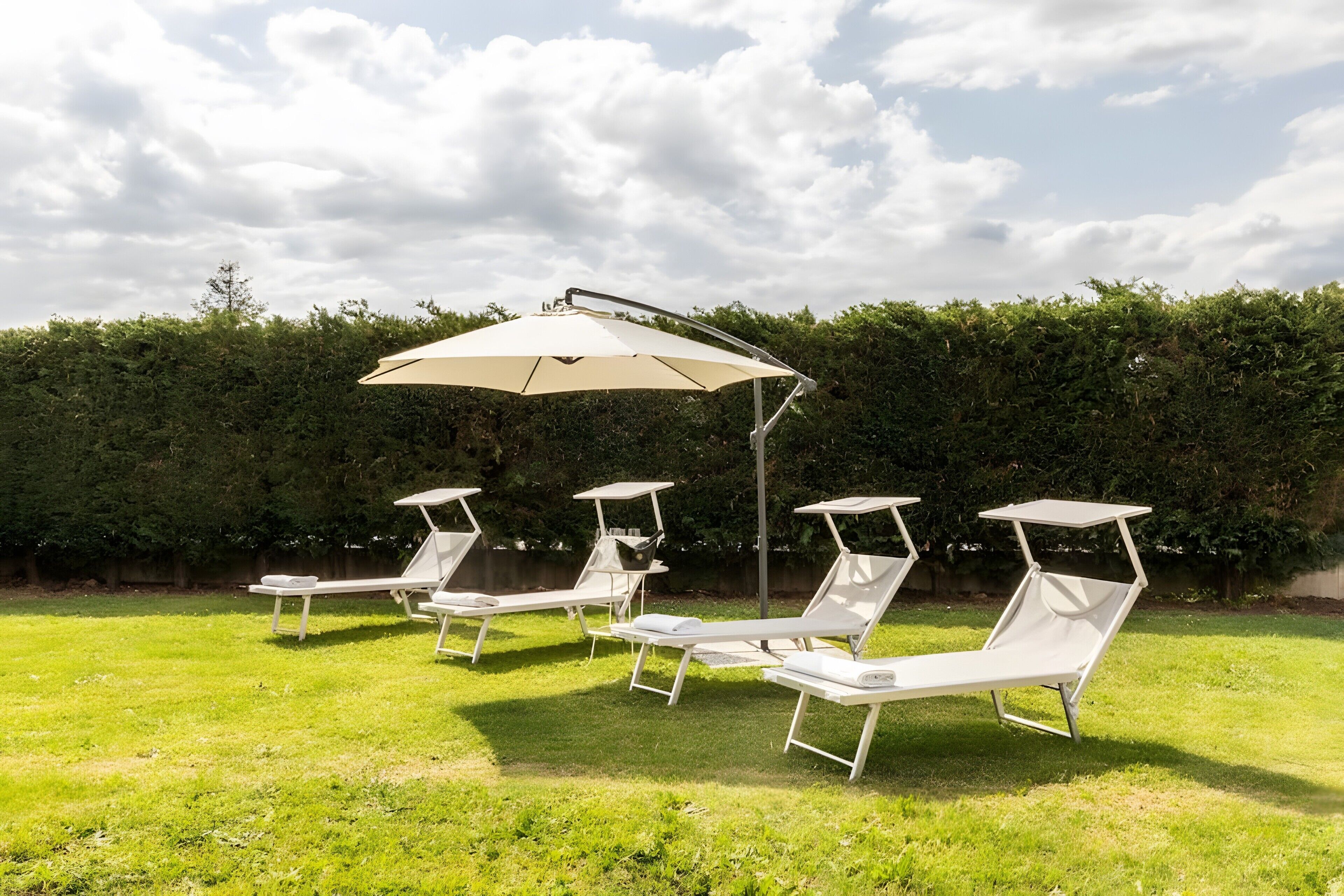 Eine Terrasse mit vier weißen Liegestühlen und einem Sonnenschirm.