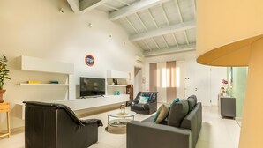 A modern living room with a sofa, a black leather chair, a television, and a 'STOP' sign on the wall. - Villa Il Fico – Cavriglia: Relax in the Heart of Chianti (Cavriglia)