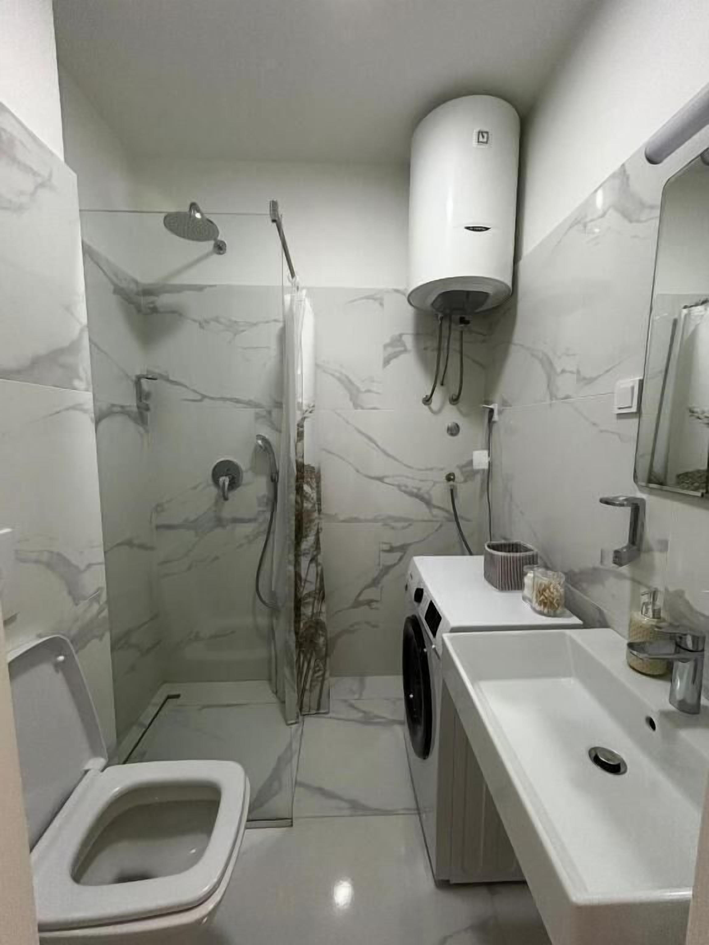 A compact bathroom with a shower, toilet, and washing machine.