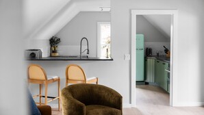 Una cocina moderna con encimera negra, paredes blancas y un mueble verde. Hay dos sillas de madera con cojines blancos.