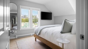 Un dormitorio con cama, una mesita, televisor y ventana con vistas.