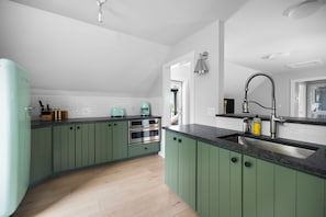 A kitchen with green cabinets, a black countertop, a stainless steel sink, and a built-in oven. - Robin's Nest in Leland (Leland)