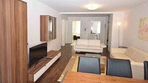 Un salon moderne doté d’un téléviseur à écran plat, d’un meuble en bois, d’un canapé beige et d’un coin repas avec une table et des chaises en bois.
