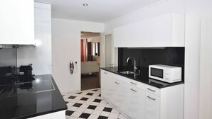 Une cuisine de taille réduite avec des meubles blancs, un plan de travail noir, un four à micro-ondes et un évier.