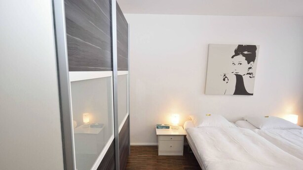 Une chambre à coucher comprenant un lit, des tables de chevet, une commode, une œuvre d’art accrochée au mur et une porte coulissante.