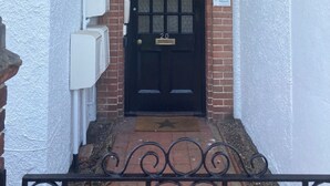 A black door with a grid pattern, a brick wall, and a white wall with a window.
