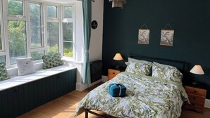 A bedroom with a bed, two bedside tables, a window with curtains, and a view of greenery outside.