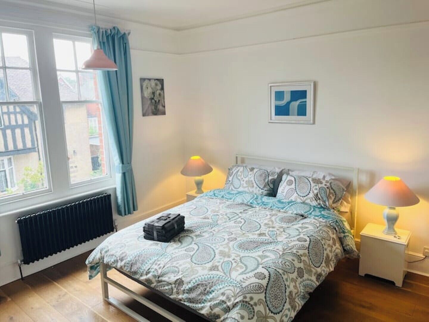 Une chambre à coucher avec un lit, deux lampes de chevet, un radiateur et une fenêtre avec des rideaux.