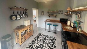 A compact kitchen with a central island, hanging pots, and a patterned rug.