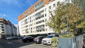 Een meerlaags woongebouw met balkons, een afgesloten parkeerterrein en een heldere lucht.