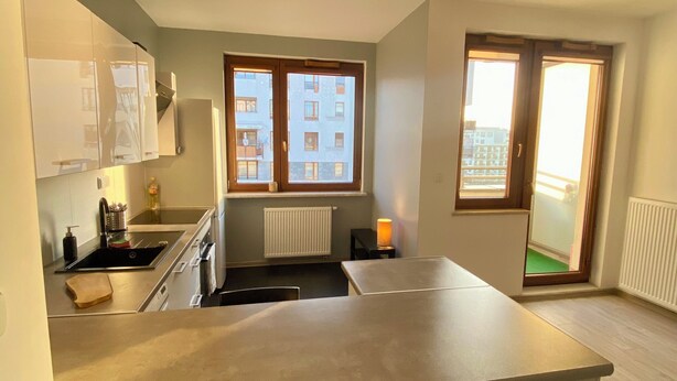 Een moderne keuken met een centraal kookeiland, een inbouwoven en een raam met uitzicht op een woonwijk.