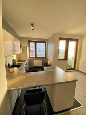 Une cuisine moderne dotée d’un îlot central, d’un four encastré et d’une fenêtre donnant sur un quartier résidentiel.
