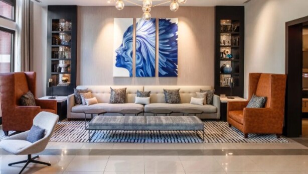 A modern living room with a sofa, armchairs, a coffee table, and a chandelier. There is a large abstract painting on the wall and a bookshelf to the left. - 1-bedroom in Arlington, DC metro area with on-site parking included (Arlington)