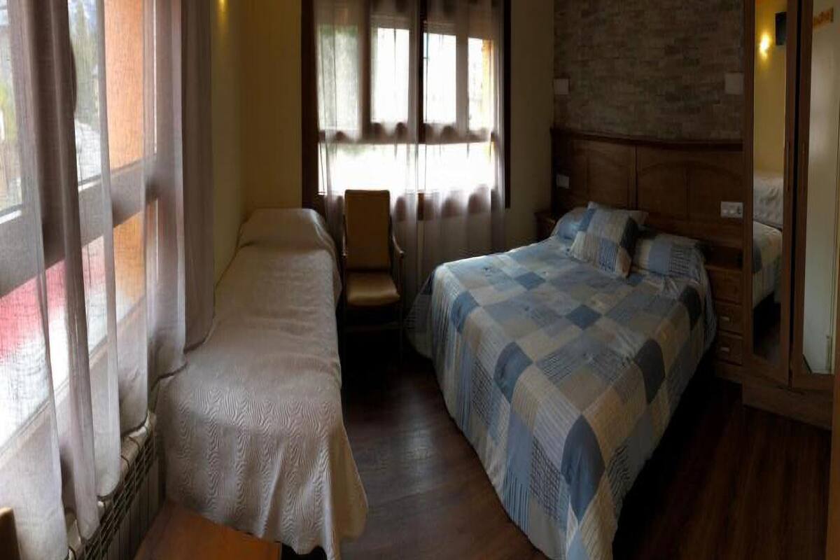 A bedroom with two single beds, a chair, and a large window with curtains.