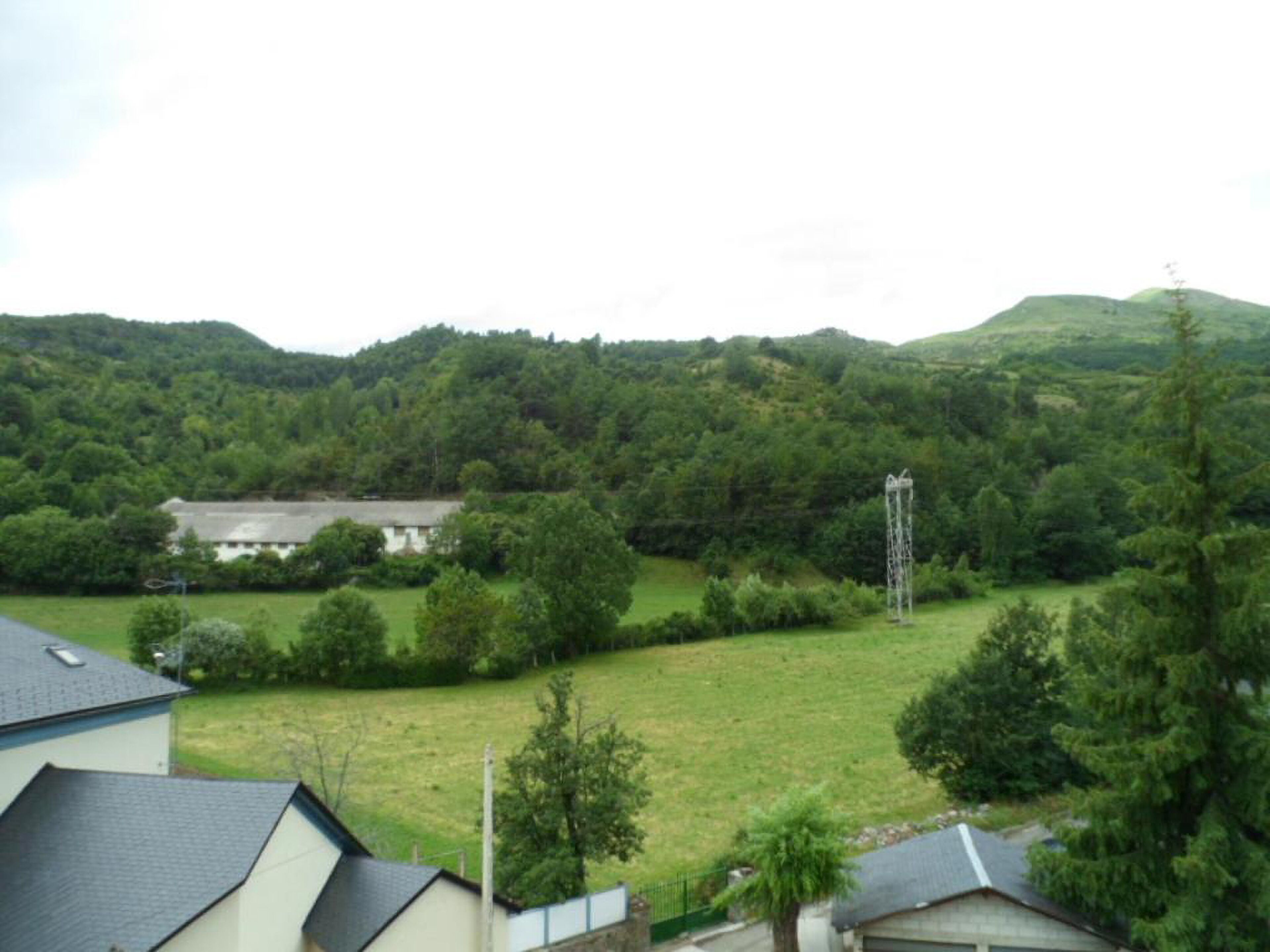 A rural landscape with a house, a field, and a hill in the background.