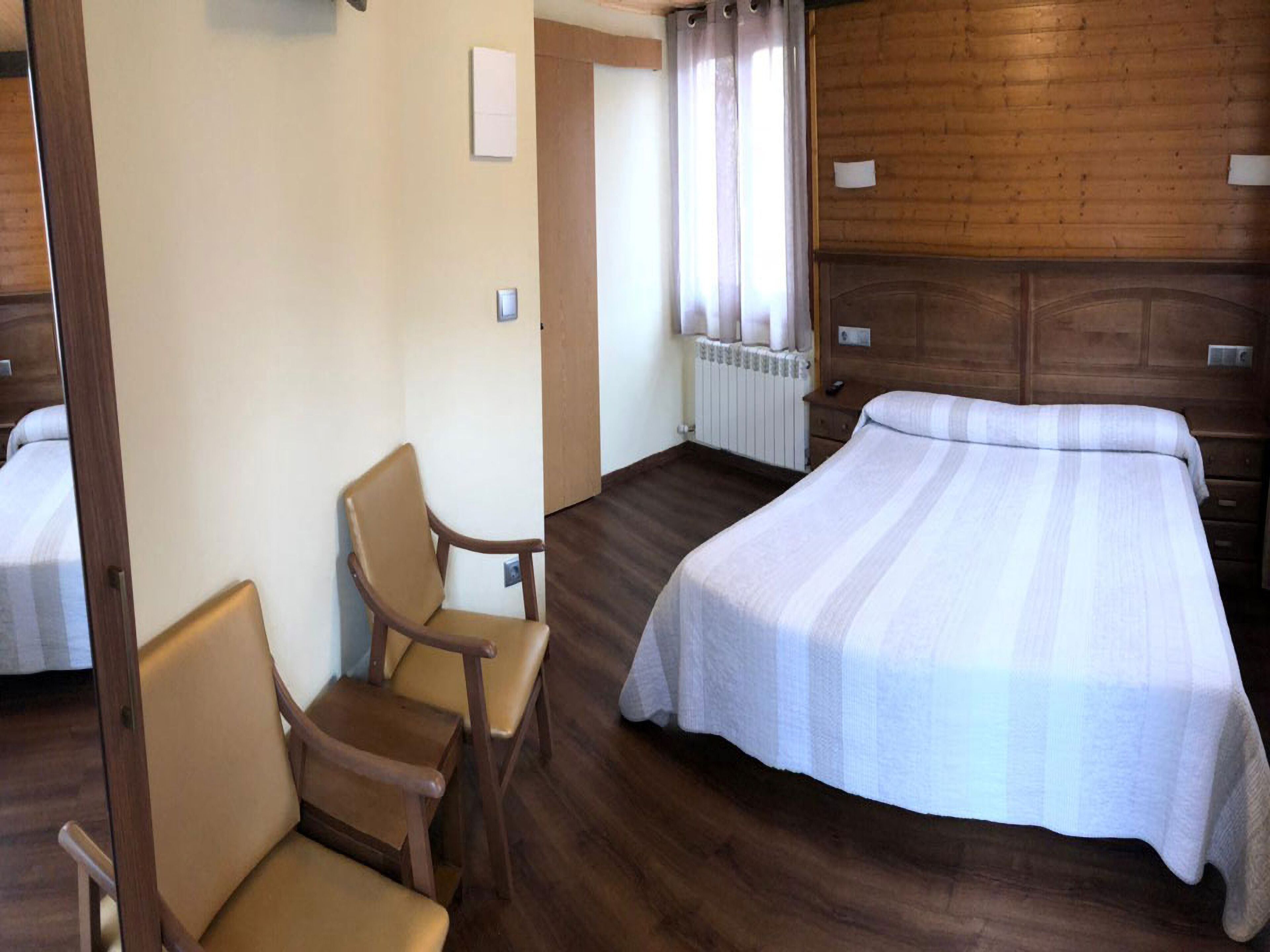 Ein Hotelzimmer mit Bett, Sessel, Heizkörper und Holzwänden.