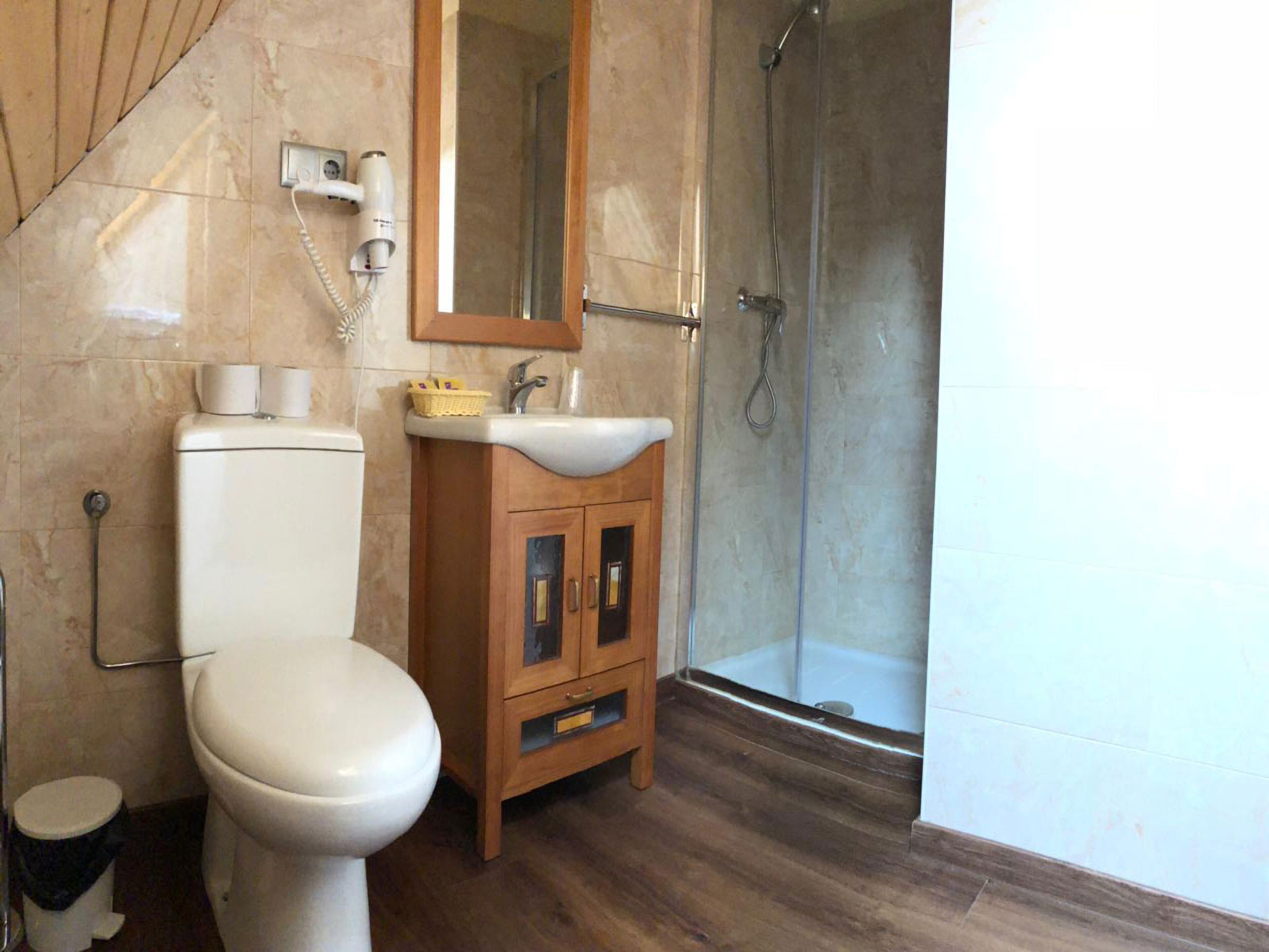 A bathroom with a toilet, sink, mirror, and shower.