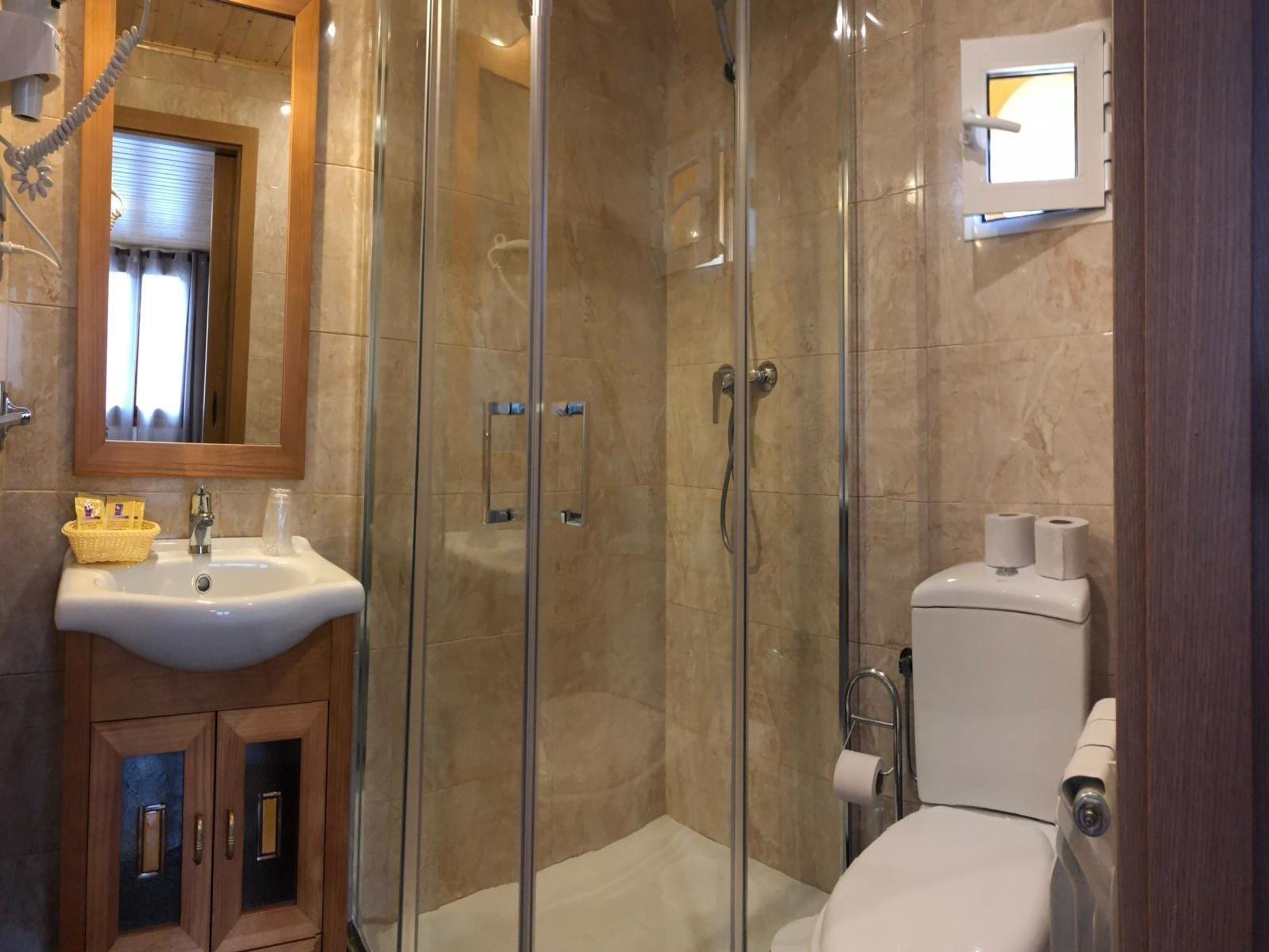 Une salle de bain dotée d’une douche à parois de verre, d’un lavabo avec un panier contenant des articles de toilette et de toilettes équipées d’un distributeur de serviettes en papier.