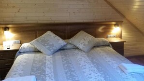 A cozy attic bedroom with a wooden sloped ceiling, a large bed with patterned bedding, two bedside lamps, and a nightstand. - Hotel Sarao 3000 (Escarrilla)