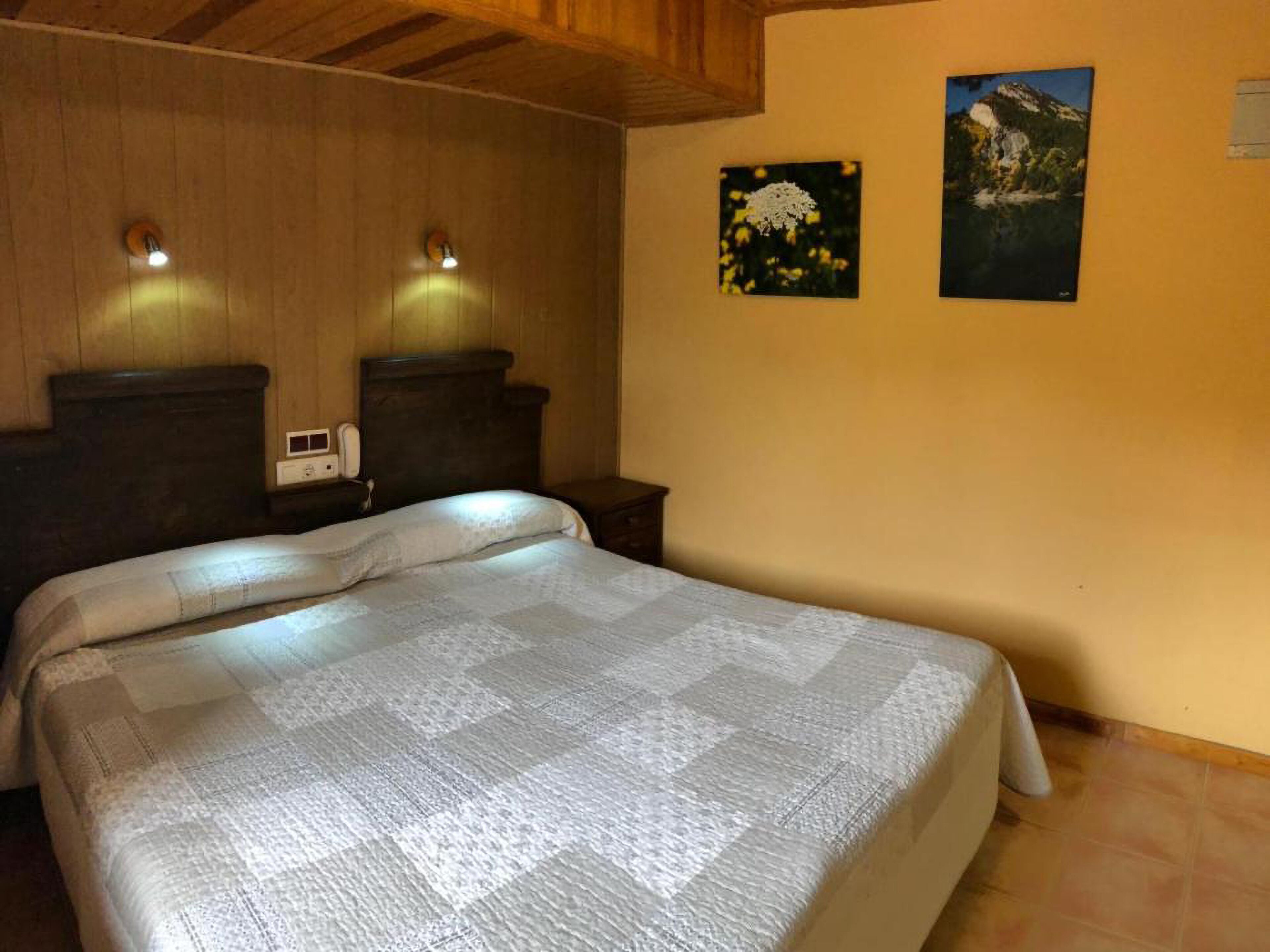 A bedroom with a large bed, wooden headboard, two bedside tables, a bedside lamp, and two framed pictures on the wall.