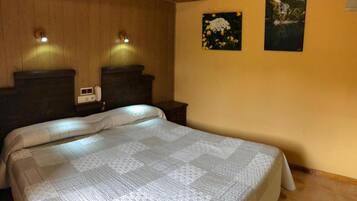 Un dormitorio con una cama grande, cabecera de madera, dos mesitas de noche, una lámpara de noche y dos cuadros enmarcados en la pared.