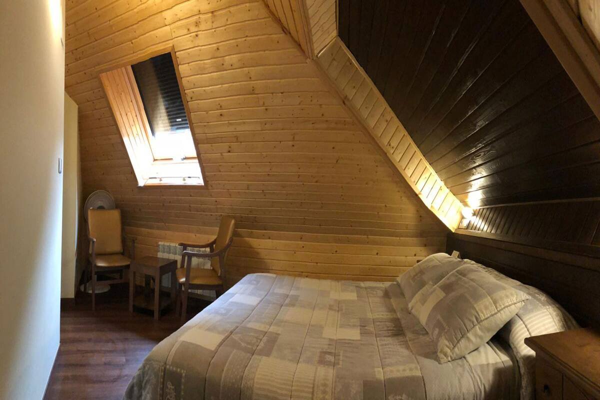 A cozy, sloped-roofed room with a bed, a chair, and a small table.