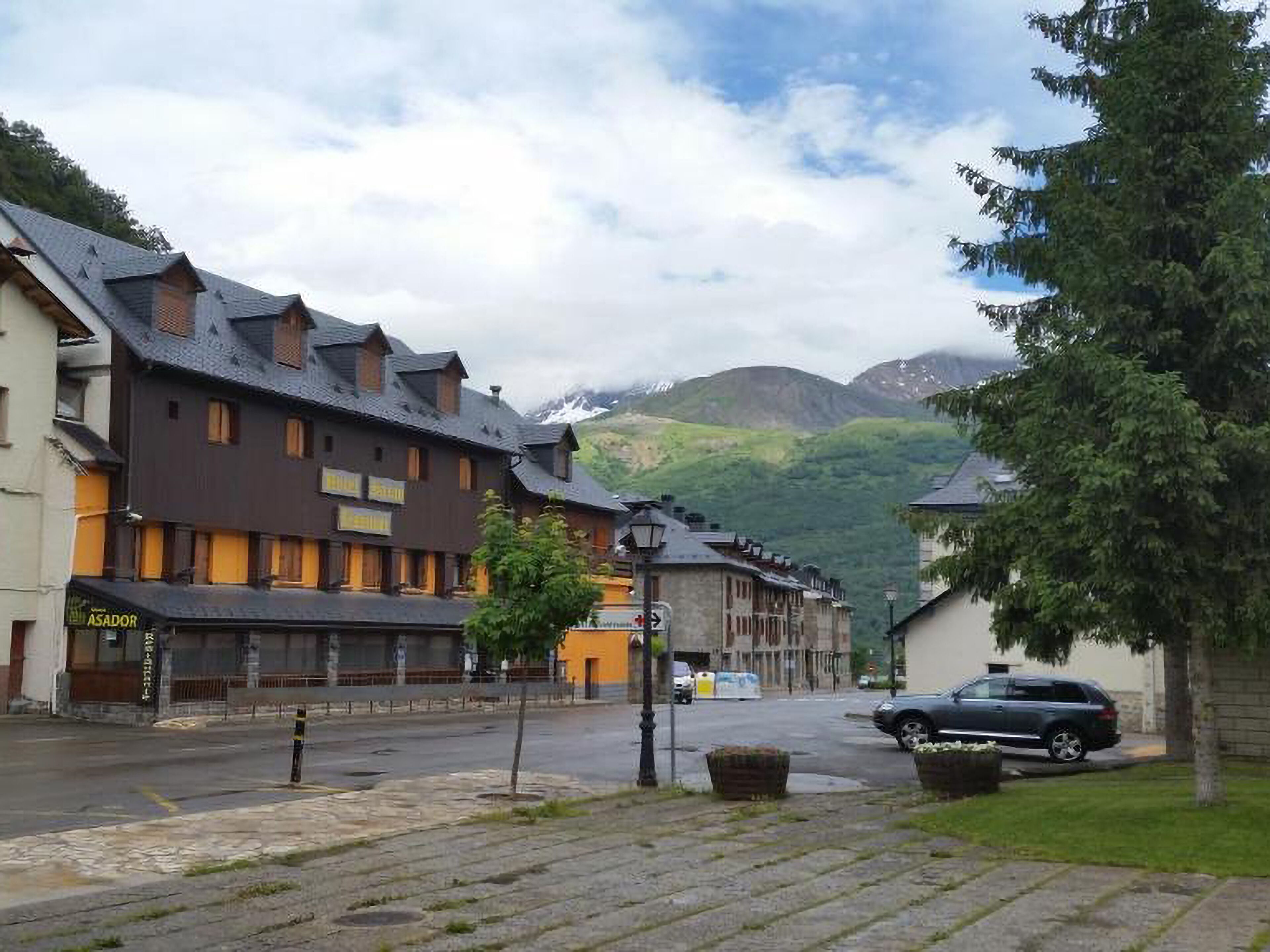Una calle con edificios tradicionales, un coche estacionado y montañas al fondo.