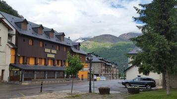 A street with traditional buildings, a parked car, and a mountain backdrop.