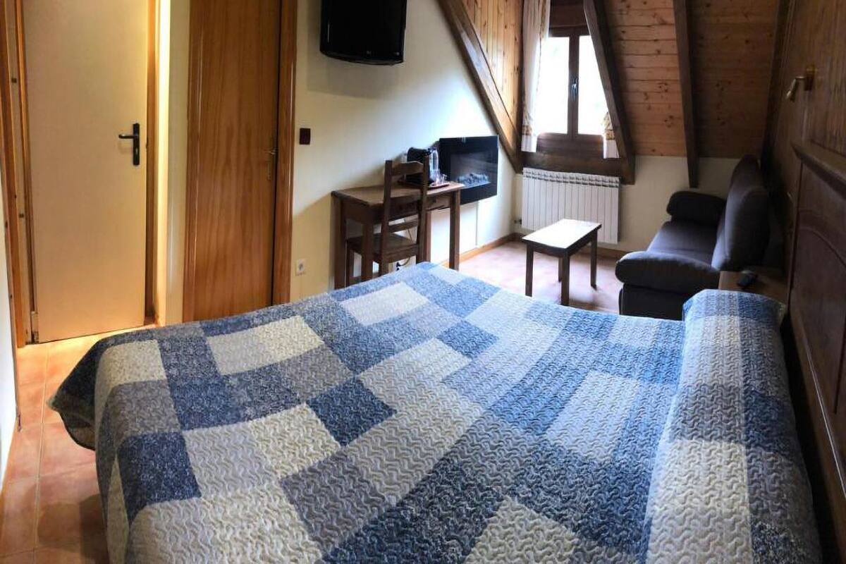 A cozy room with a large bed, a desk, a chair, and a television.