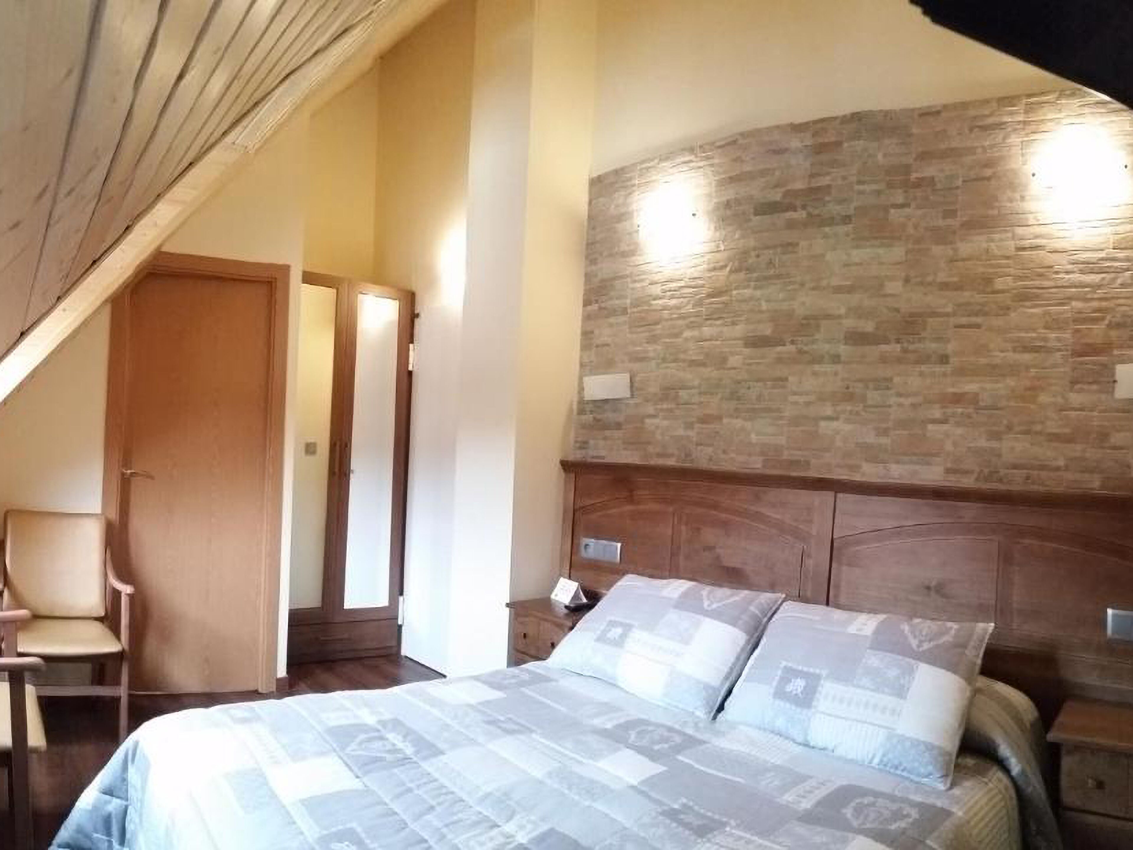 Un dormitorio con una cama grande, cabecera de madera, pared de piedra y una silla.