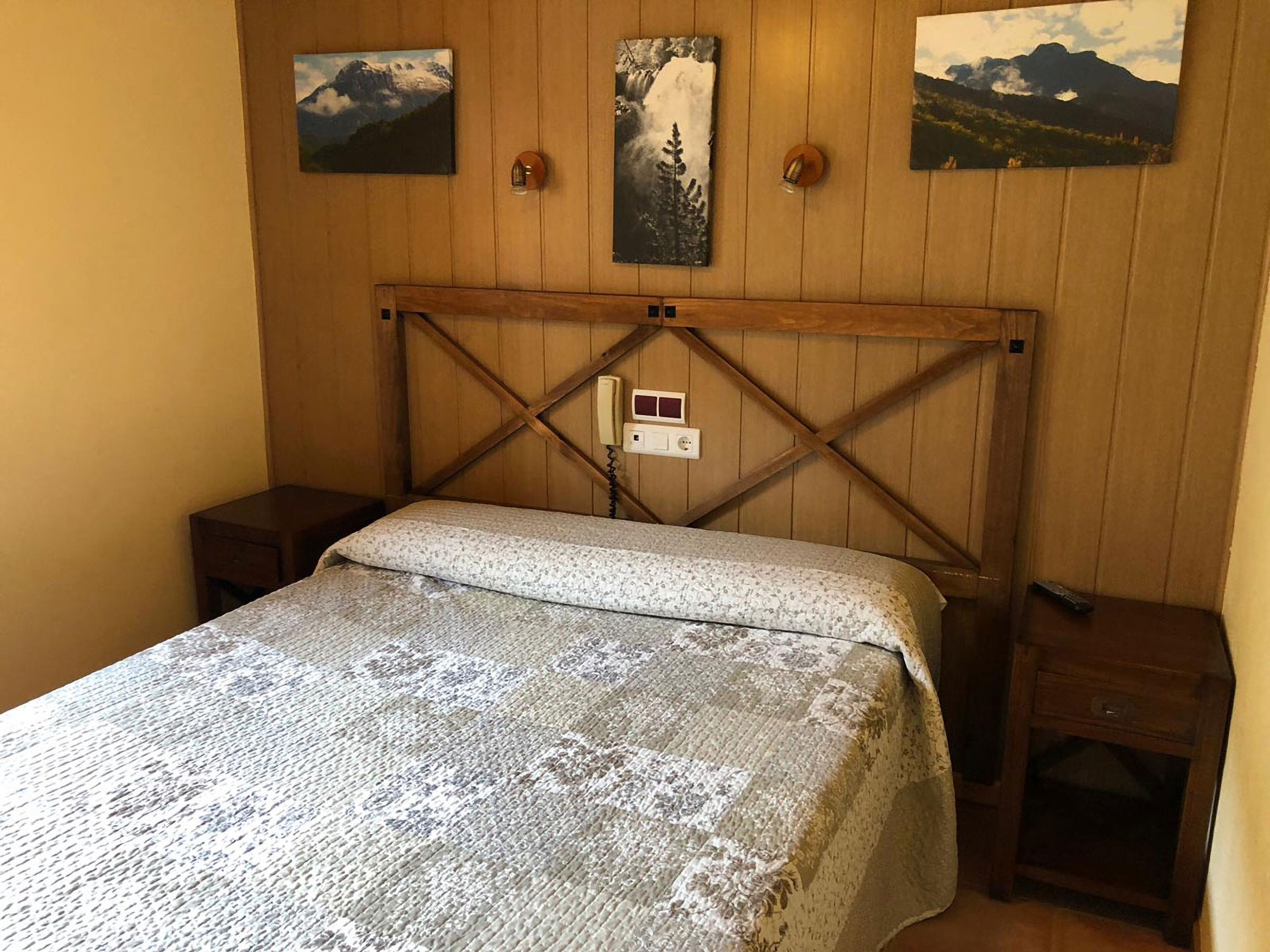 Een kamer met houten lambrisering, een bed, twee nachtkastjes en drie landschapsschilderijen aan de muur.