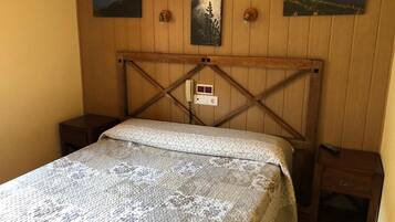 Een kamer met houten lambrisering, een bed, twee nachtkastjes en drie landschapsschilderijen aan de muur.