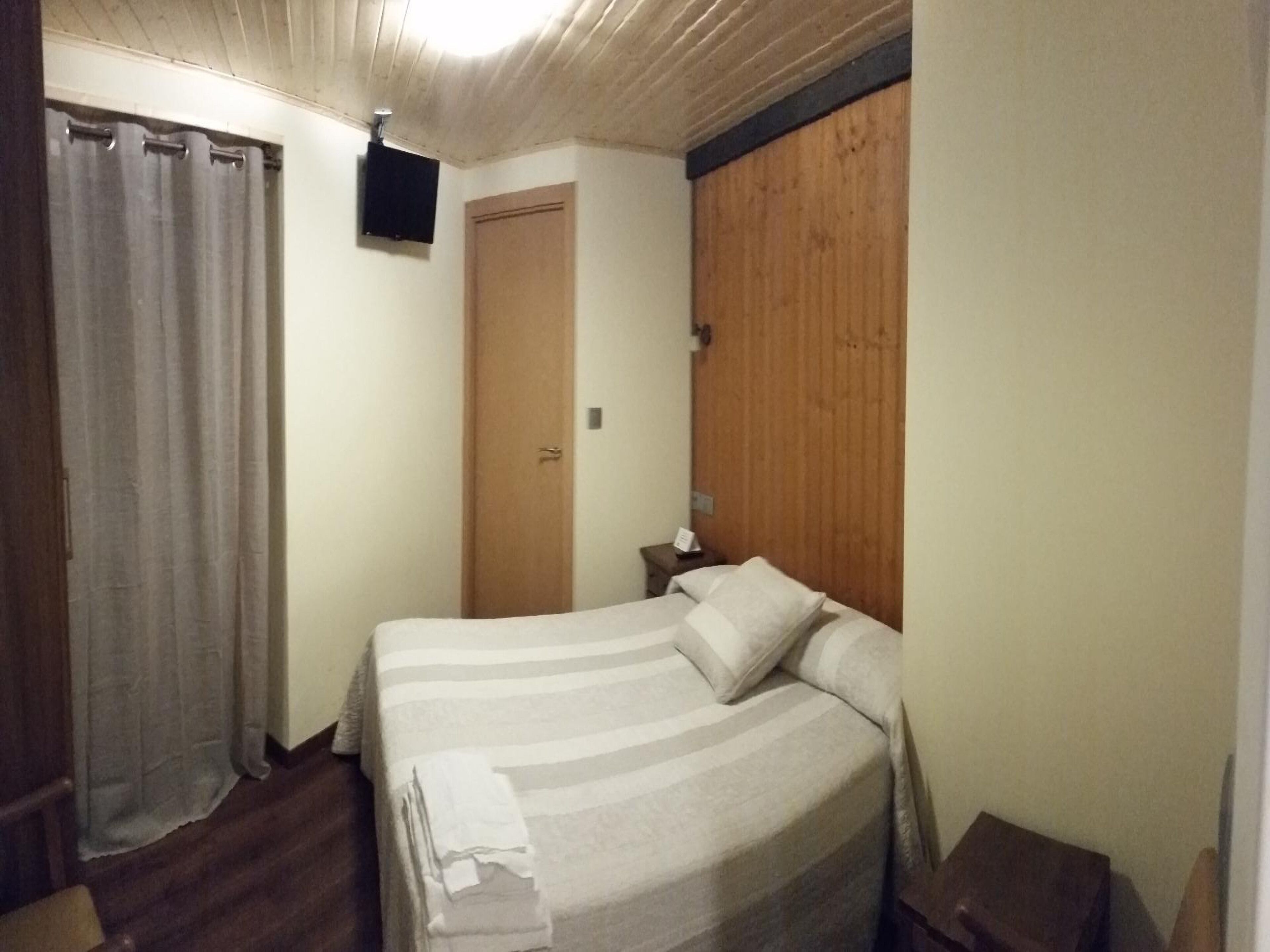 Un dormitorio con una cama, una puerta de madera, una mesita de noche y un televisor montado en la pared.