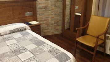 A bedroom with a wooden headboard, a quilted bedspread, a wooden nightstand, a chair, and a stone-textured wall.