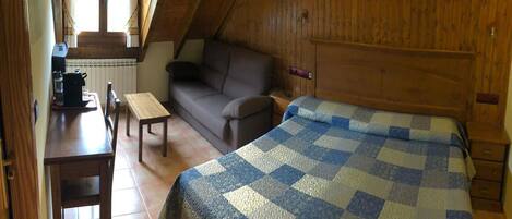 Un cuarto ático acogedor con techo inclinado de madera, una cama con colcha de cuadros, un sofá, una mesita y una silla.